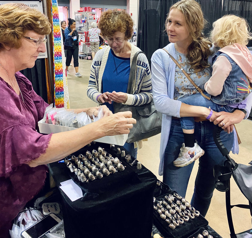 Customers exploring a collection of heirloom quality sterling silver thimbles at a craft fair.