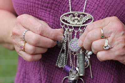 Hands holding a vintage silver chatelaine with various sewing tools and thimbles, highlighting heirloom quality accessories.