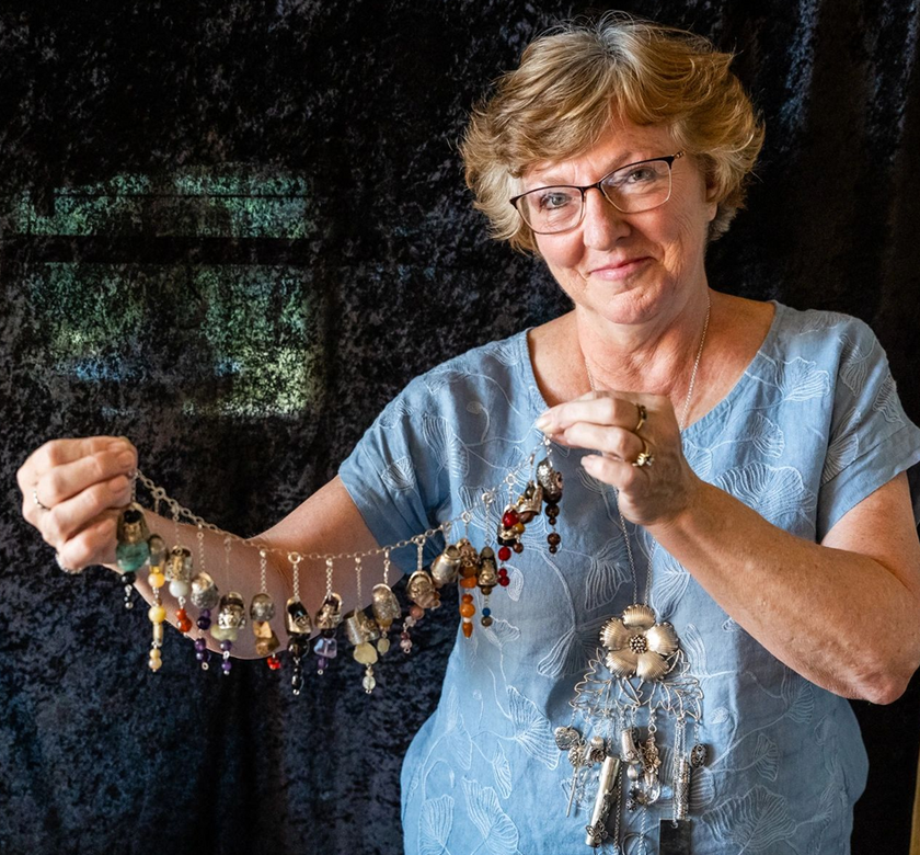 Woman displaying a collection of decorative thimbles on a chain, showcasing sewing accessories and heirloom thimble designs.
