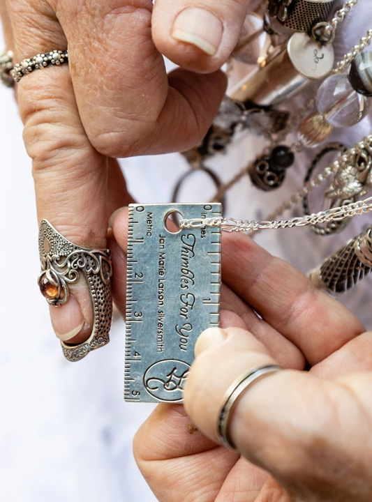 Close-up of hands holding a silver ruler pendant with engraving, showcasing unique jewelry design.