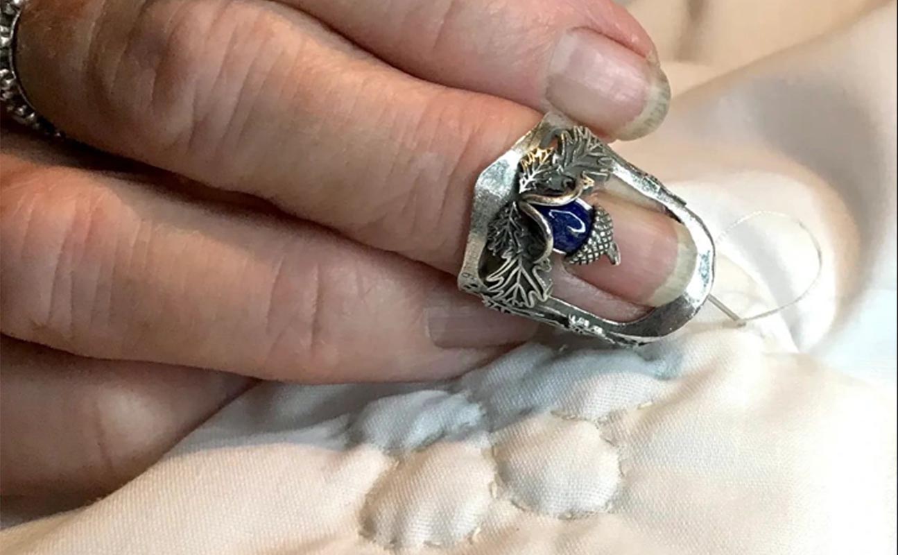 Close-up of a handmade silver thimble with decorative design, used for sewing on fabric.