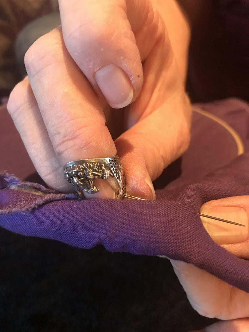 Hand sewing fabric with a Chicken, Hen, Rooster Thimble, showcasing sterling silver thimble craftsmanship and sewing tools.