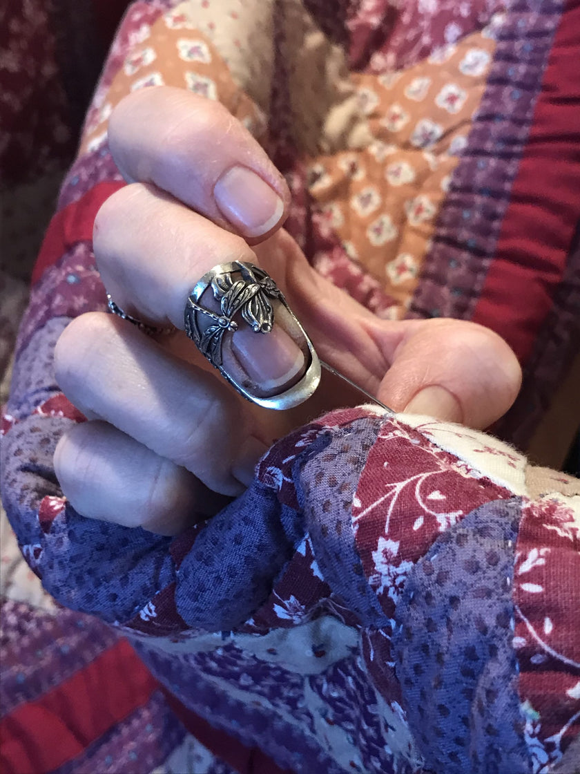 Dragonfly and Iris Thimble displayed on a hand, surrounded by a colorful quilt for crafting enthusiasts.