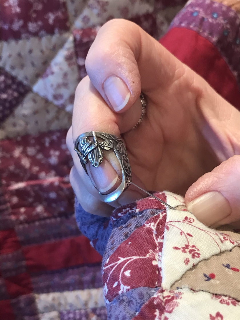 Hand using the Dragonfly and Iris Thimble for quilting on a patchwork quilt.