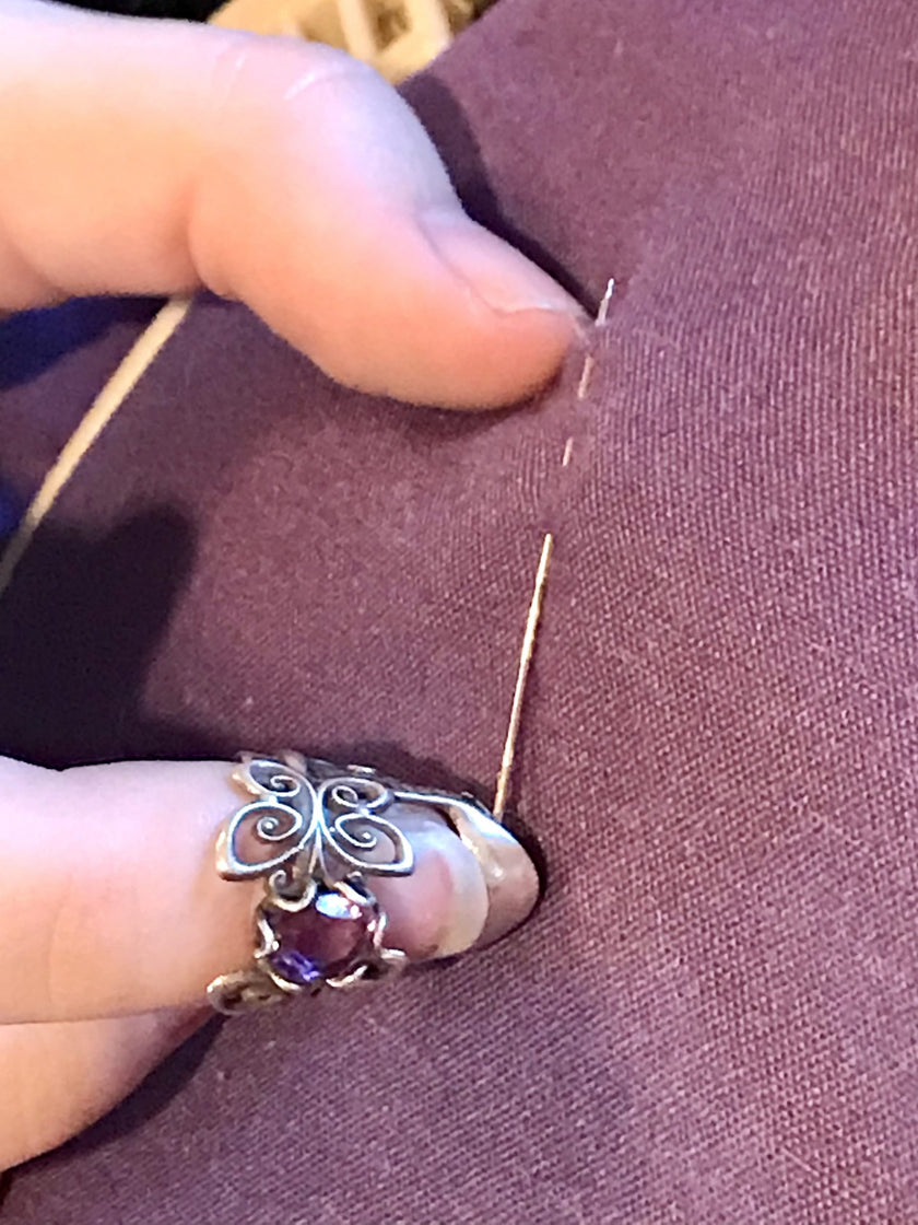 Close-up of a hand using a Butterfly Short Thimble for sewing on purple fabric, showcasing the sterling silver thimble design.